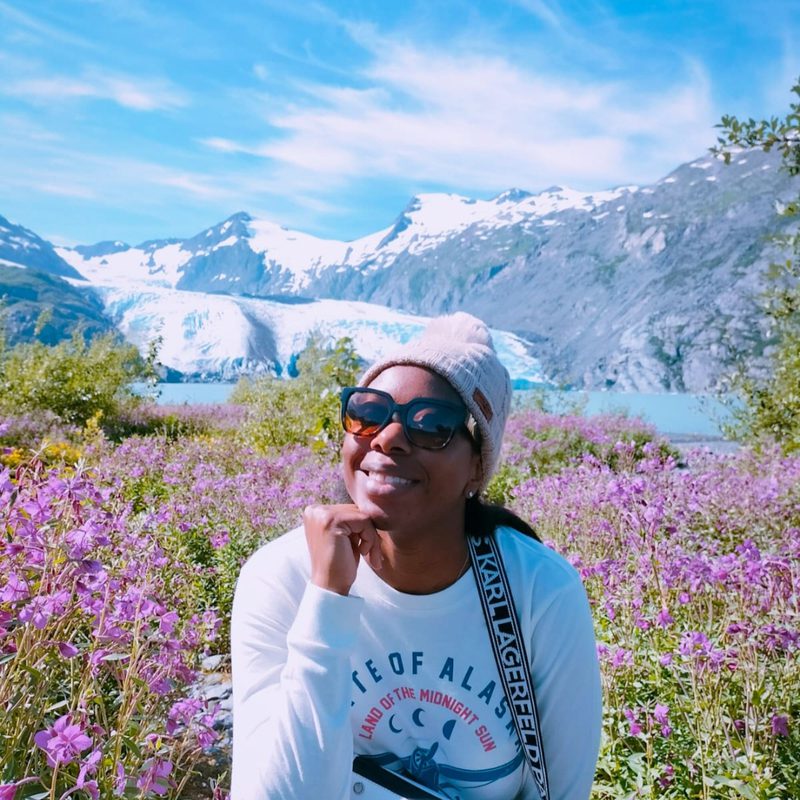 Hayley Molefe in a field of wildflowers below an Alaskan glacier
